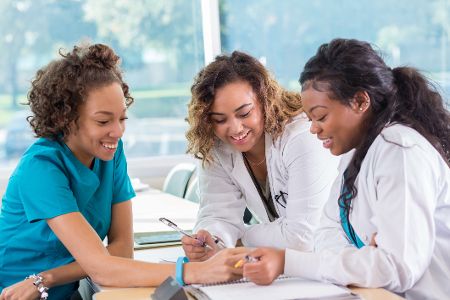 Mehrere Frauen in Krankenhauskleidung schauen gemeinsam Dokumente an