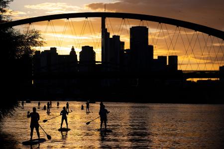 Bei Sicht auf die Skyline im letzten Licht des Tages fahren Stand-Up-Paddler in Nähe der Frankfurter Osthafenbrücke über den Main.