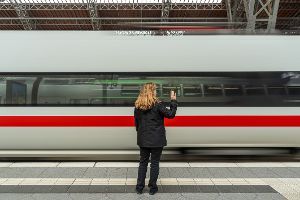 Frau steht vor abfahrendem Schnellzug und winkt