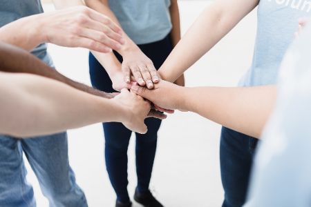 Menschen stehen im Kreis und strecken ihre ausgestreckten Arme zu einer Faust in der Mitte zusammen