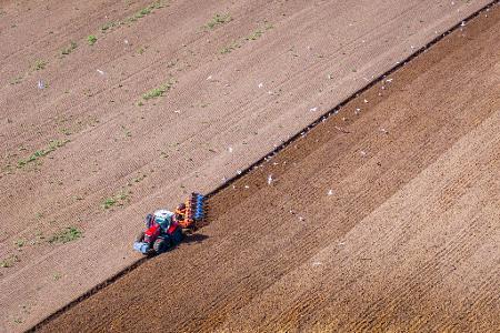 In Medewege zieht ein Traktor einen Pflug über einen Acker und bereitet den Boden für die nächste Aussaat vor. 