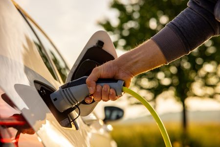 Mensch steckt Stecker in Elektroauto