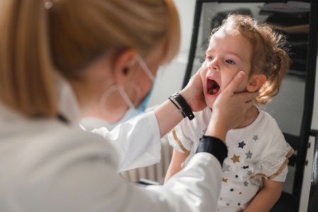 Ärztin untersucht kleines Kind mit weit geöffnetem Mund