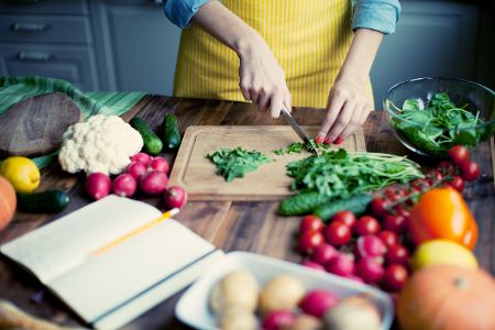 Frau schnippelt Gemüse vor offenem Rezeptbuch