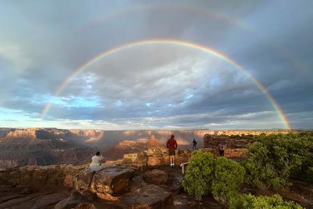 Menschen versammeln sich an einem Aussichtspunkt, als ein doppelter Regenbogen über dem Dead Horse Point State Park in der Nähe von Moabin den USA erscheint, nachdem die Sonne aufgegangen und ein Gewitter vorbeigezogen ist.