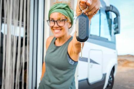 Happy new buyer owner of camper van motorhome show at the camera her keys with happiness. New house and vehicle for vacation concept scene. Travel vanlife lifestyle. Adventure. Nomadic people female