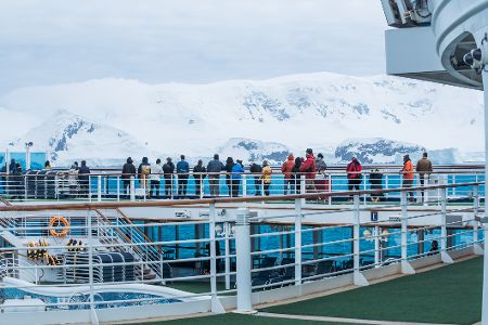 Passagiere eines Schiffes stehen an der Reling und schauen auf Packeis hinunter