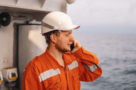 Arbeiter steht an der Reling eines Schiffes auf hoher See und telefoniert