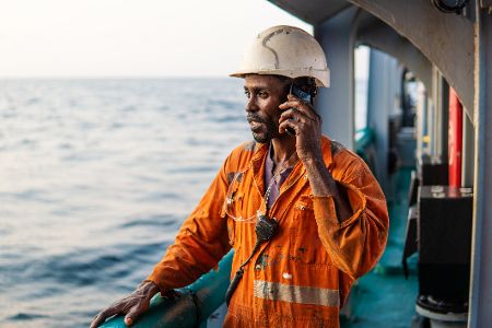 Arbeiter steht an der Reling eines Schiffes auf hoher See und telefoniert