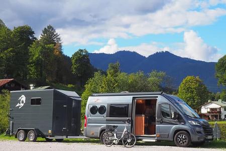 Gray camper van with a horse trailer in a parking lot