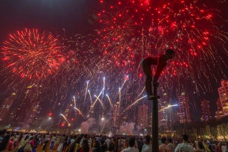 Ein Mädchen performt auf einer Mallakhamb-Stange, während Feuerwerkskörper den Himmel während des Diwali-Lichterfestes in Mumbai erhellen.