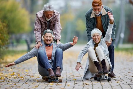 Zwei alte Männer schieben zwei alte Frauen auf Skateboards durch den Park