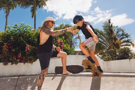 Älterer langhaariger Mann hilft einem kleinen Jungen in einem Skatepark die Rampe hoch