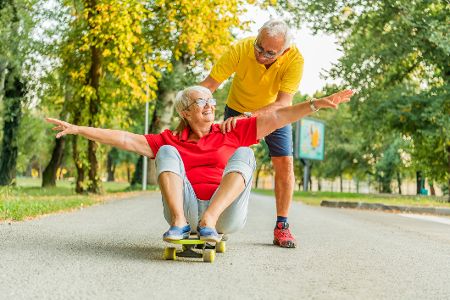 Älterer Mann schiebt seine Frau auf einem Skateboard durch den Park