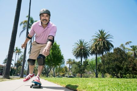 Älterer Mann fährt freudestrahlend eine Straße auf einem Skateboard hinunter