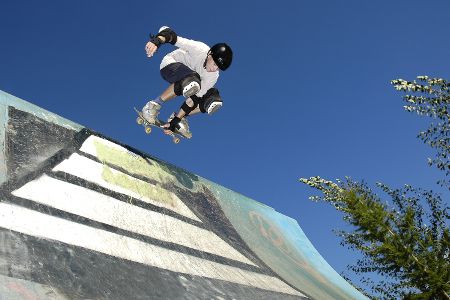 Skater mit Schutzkleidung springt in einer Halfpipe