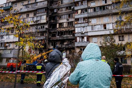 Menschen beobachten die Arbeit der Feuerwehr in einem zerstörten Wohnhaus nach einem russischen Drohnenangriff.