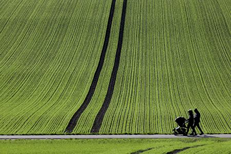 Spaziergänger gehen im Sonnenschein an einem frisch bestellten Feld in Baden-Württemberg vorbei.