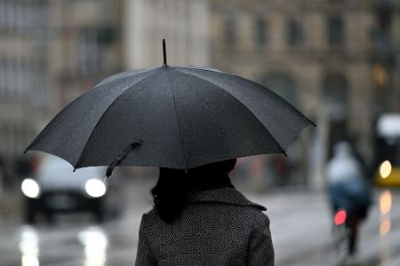Eine Frau geht mit einem Regenschirm durch Berlin Mitte.