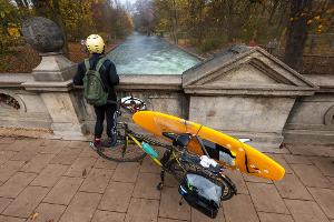 Ein Mann mit einem Surfboard an seinem Fahrrad schaut von einer Brücke auf die - nicht mehr vorhandene - Eisbachwelle im Englischen Garten.