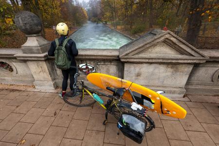 Ein Mann mit einem Surfboard an seinem Fahrrad schaut von einer Brücke auf die - nicht mehr vorhandene - Eisbachwelle im Englischen Garten.