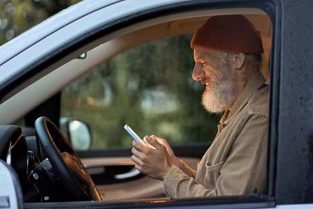 Happy older man traveler sitting in camper van using mobile in camping.