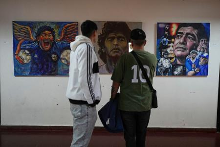 Menschen betrachten eine Kunstausstellung mit Bildern des verstorbenen Fußballstars Maradona.