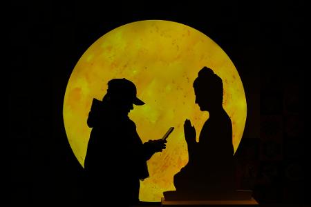 "Zwiegespräch":  Eine Frau surft auf ihrem Smartphone vor einer Buddha-förmigen Pappfigur, die in einem Einkaufszentrum in Peking aufgestellt ist.