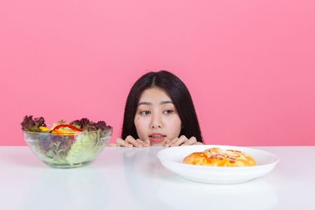 Frau schaut auf einen Teller mit Salat versus einen mit Pizza