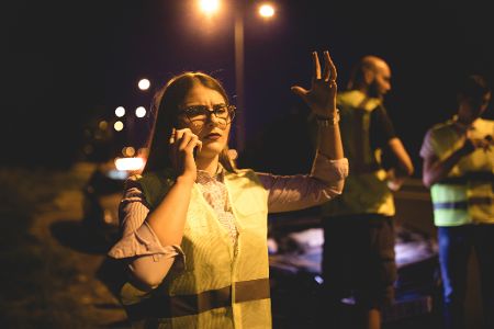 Frau in Warnweste ruft nach Unfall mit dem Handy Hilfe.