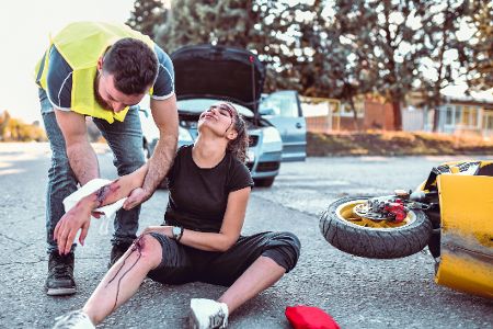 Schwer verletzte Frau sitzt nach Unfall auf der Straße und wird von einem Helfer versorgt