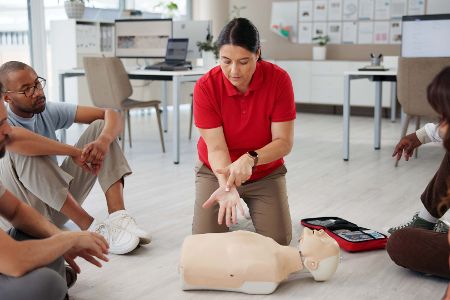 Frau führt vor, wo man bei einem Dummy die Hand zur Herz-Druck-Massage anlegen muss