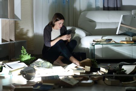 Frau sitzt nach einem Einbruch in ihrer verwüsteten Wohnung und ruft die Polizei