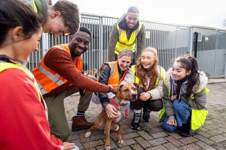 Gruppe von Teenagern in Warnwesten bekommt von einem Erwachsenen etwas an einem Hund erklärt