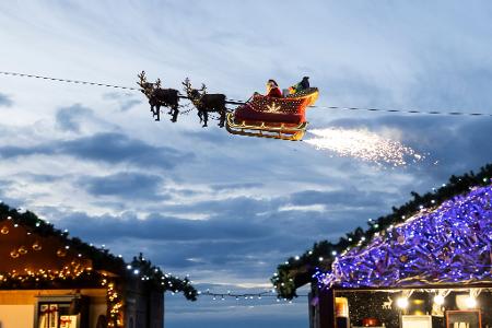 Ein Weihnachtsmann in einem fliegenden Schlitten ist in Montreux über den Weihnachtsständen vom Weihnachtsmarkt unterwegs.