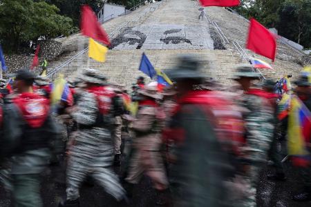 Mitglieder der Bolivarischen Miliz marschieren vor einer Treppe in Caracas, auf der die Augen des verstorbenen Präsidenten Hugo Chavez abgebildet sind, während einer Demonstration zum Gedenken an den Jahrestag der Schlacht von Santa Ines, die während des venezolanischen Bundeskriegs im 19. Jahrhundert stattfand.