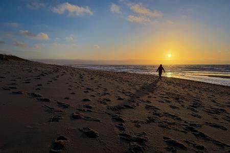 Eine Frau geht im Licht der tief stehenden Sonne am Strand bei Rantum auf Sylt spazieren.