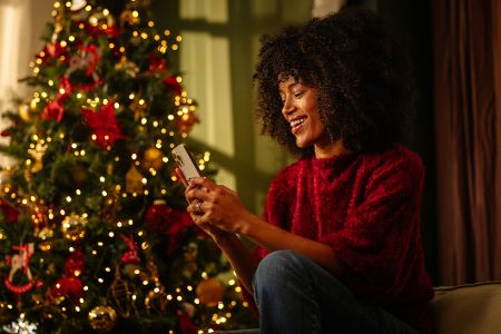 Frau nutzt Handy unterm Weihnachtsbaum