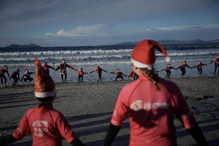 Mit Weihnachtsmannmützen verkleidete Menschen surfen während der "Papanoelada Surfera" (Surfer-Nikolaus-Aktion) am Strand von Patos. 