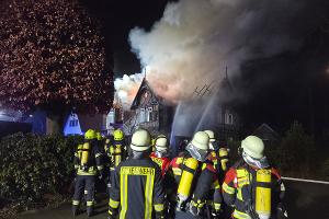 Mehrere Einsatzkräfte stehen vor dem brennenden Gebäude