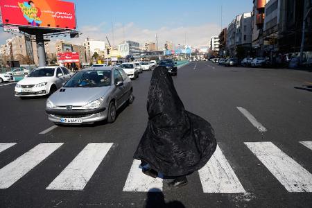 Alltag in Teheran:  Verschleierte Frau überquert Kreuzung im Zentrum