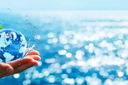 Hand hielt einen digitalen Erdball, im Hintergrund ist das Meer zu sehen