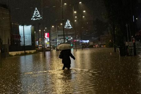 Eine Frau geht während eines Regenschauers über eine überflutete Straße in Athen.